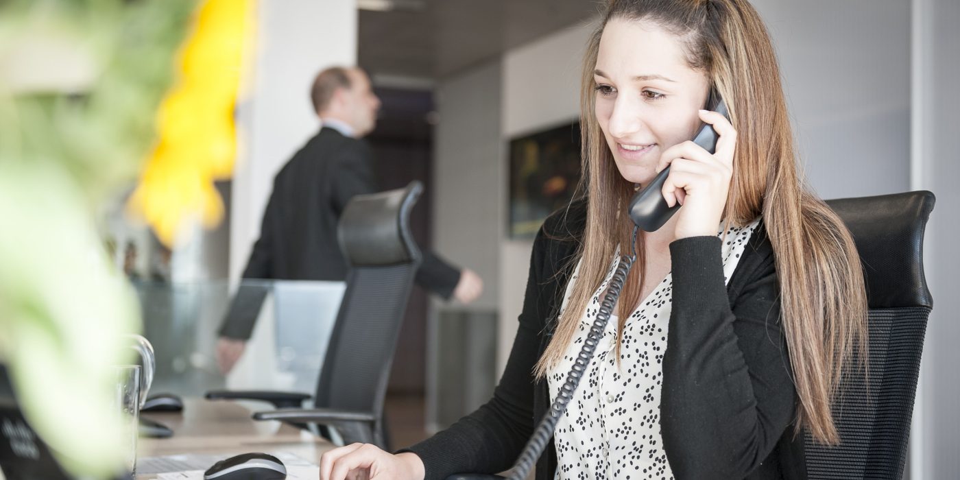 Young woman at reception desk holding telephone