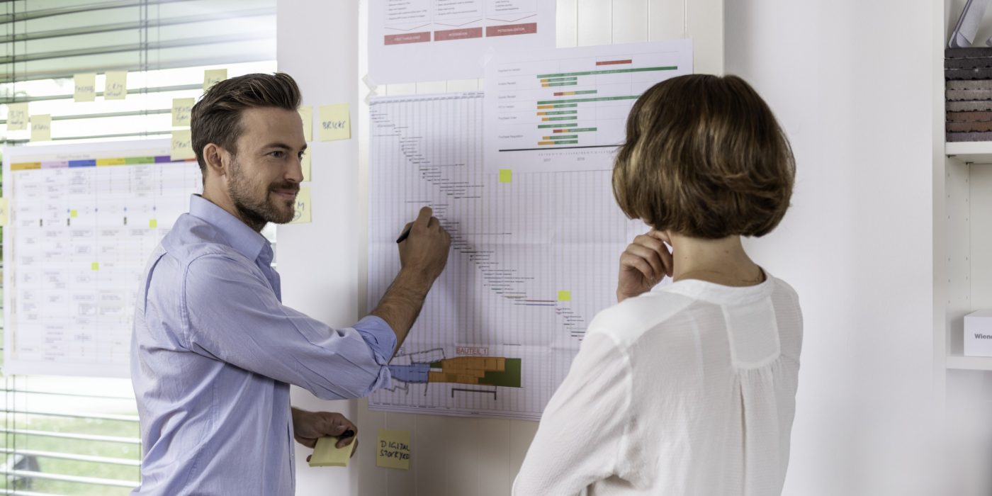 Male and female project manager in front of timeline sheets or project process maps at office