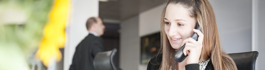 Young woman at reception desk holding telephone