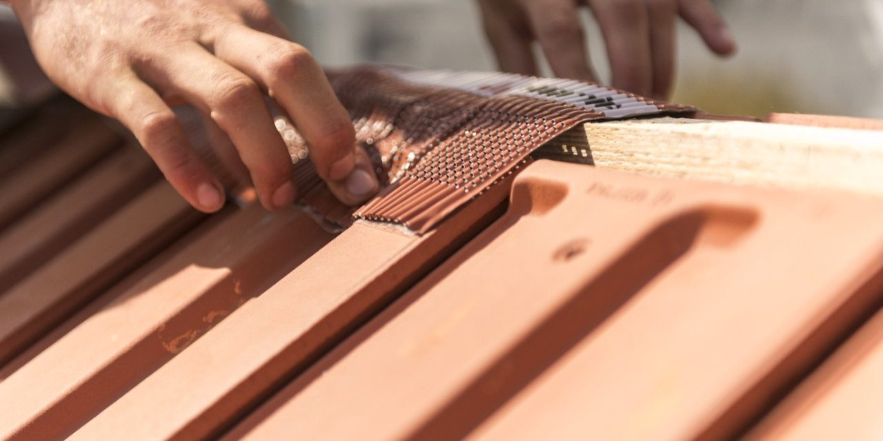 Roofer applying Alu-Grip Rol ridge and hip roll on ridge with bare hands