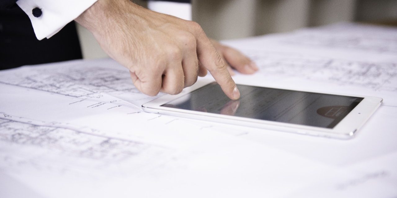 Hand typing on tablet computer lying on blueprint
