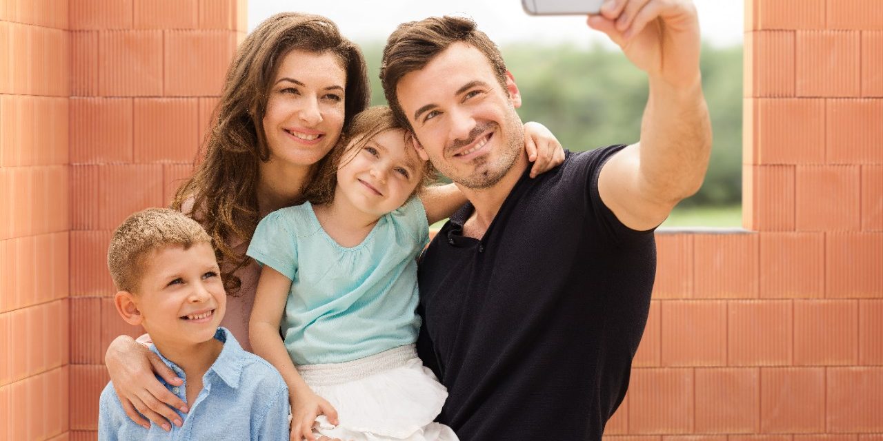 Parents with two kids taking a selfie with mobile phone inside new built house in front of bare clay block walls