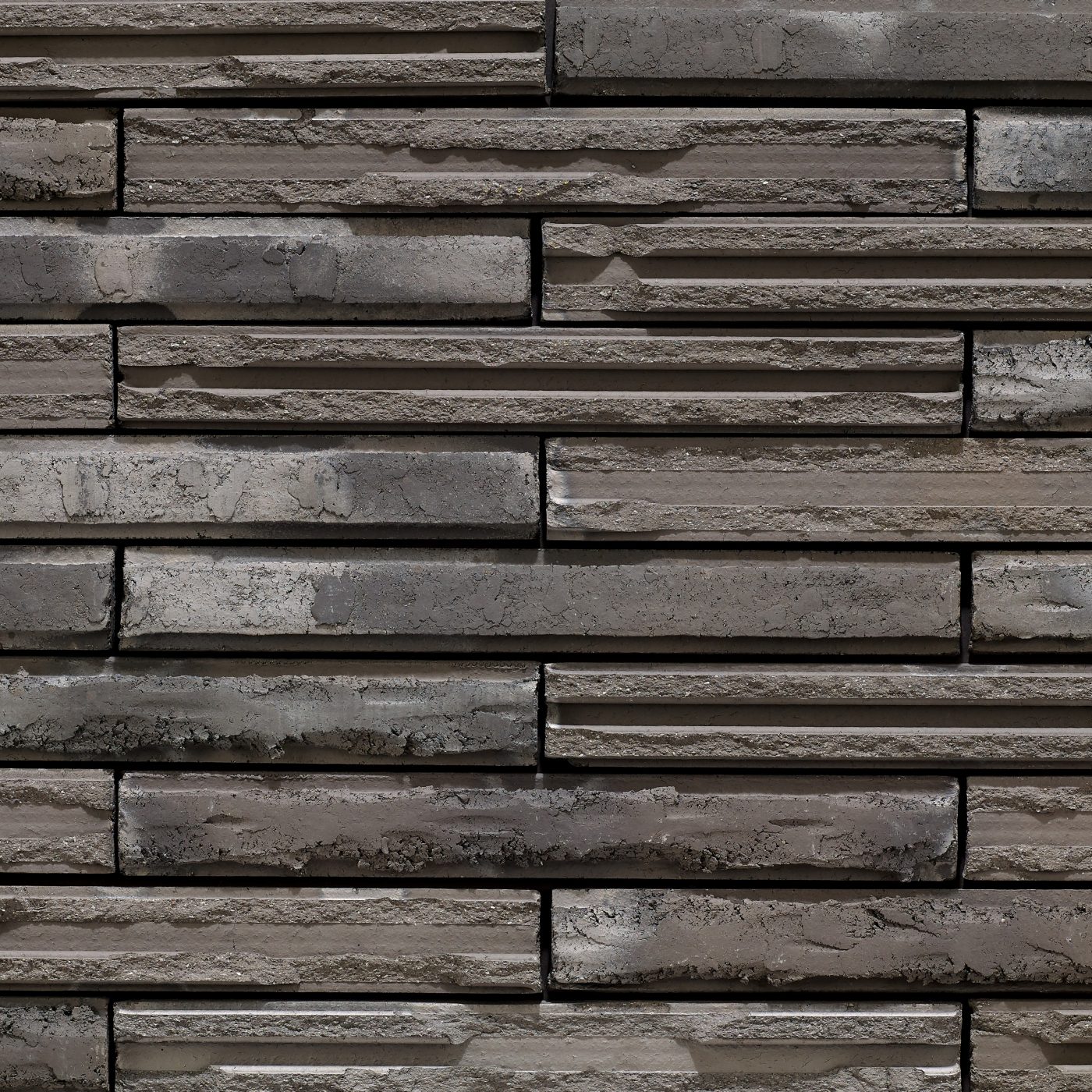 Tekstura cegieł i płytek klinkierowych Terca Cassia Long Graphite. Produkt o nietypowym wydłużonym formacie, który z łamaną fakturą lica tworzy wyjątkowe możliwości kształtowania elewacji. Kolor grafitowy.